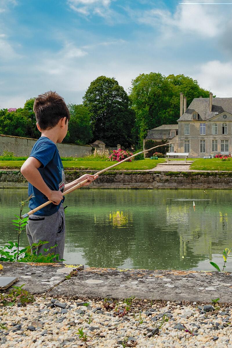 Un petit garçon pêche dans l'étang du camping le Château de Martragny