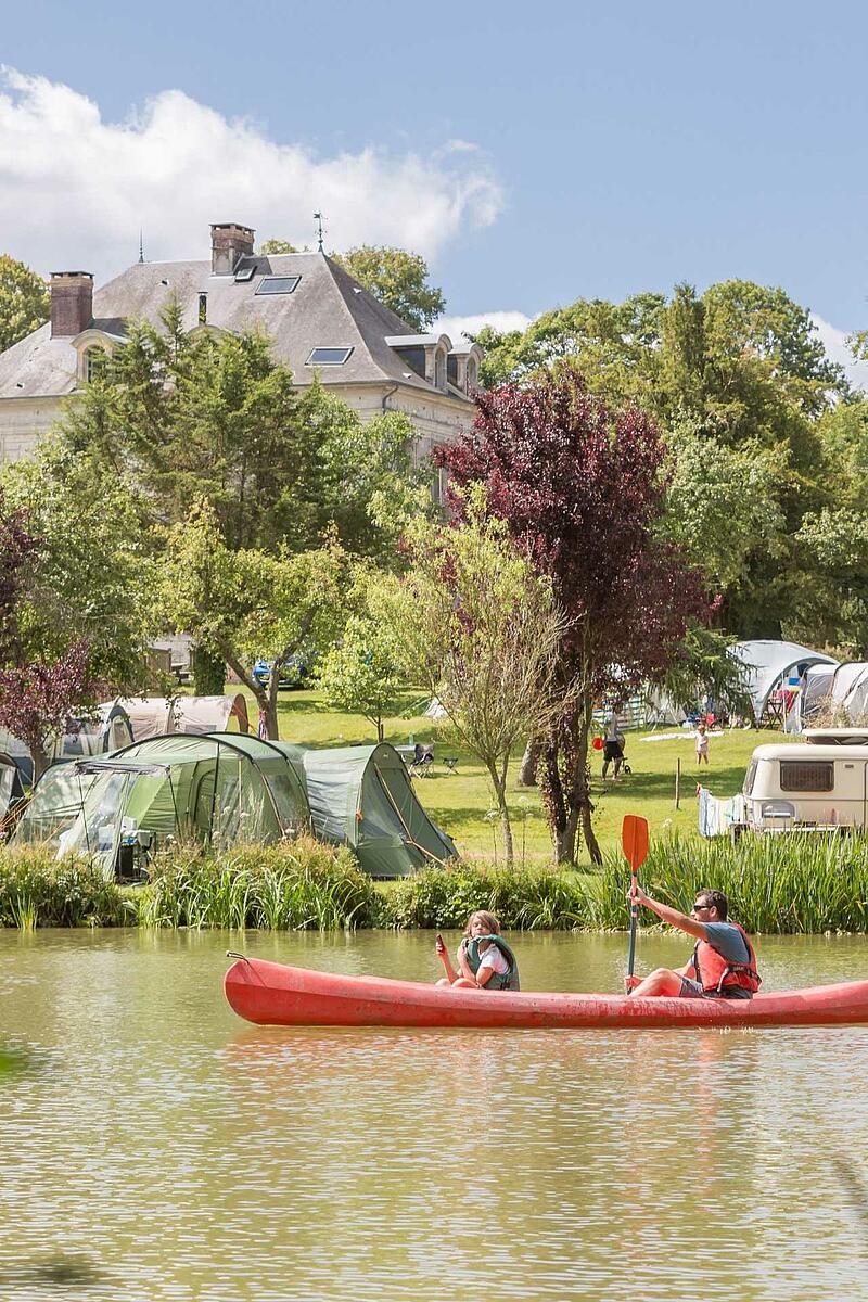 [Translate to Allemand:] Vacances en camping en France : balade en canoë sur une rivière devant un domaine avec château et tentes