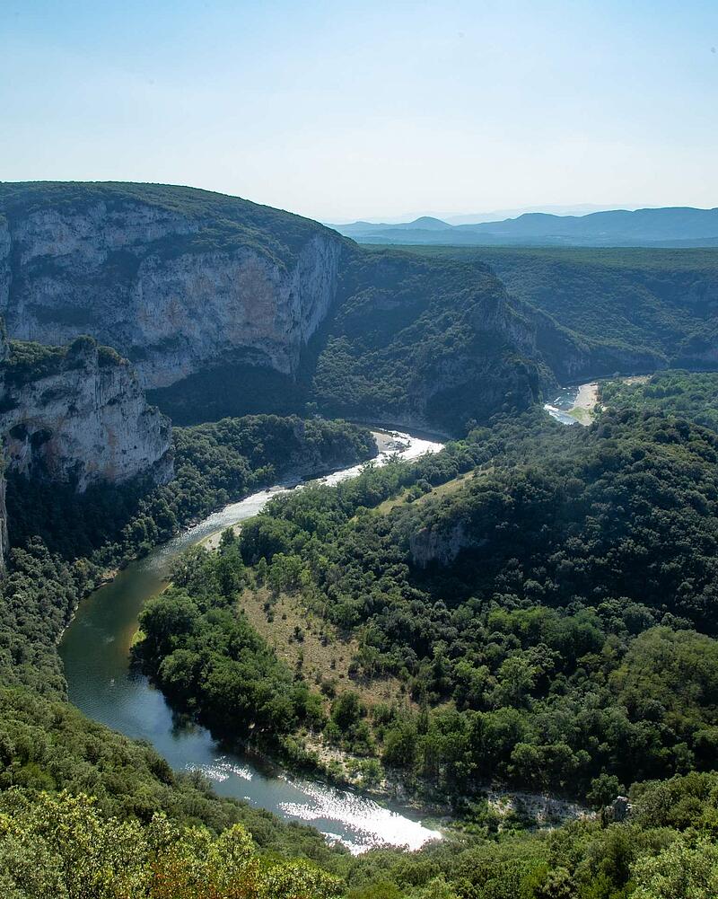 [Translate to Allemand:] Panoramic high angle view of the green Ardeche river canyon winding through deep forests and massive stone cliffs near Les Castels campsites.