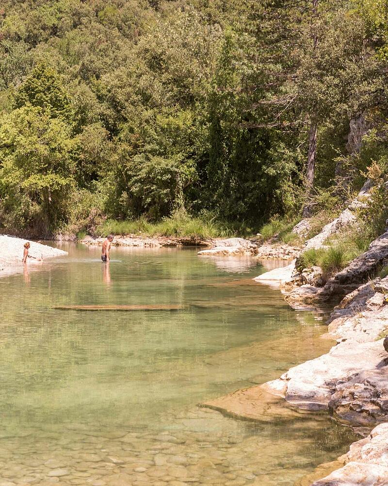 [Translate to Allemand:] People relaxing and swimming in the clear waters of a wild river near Les Castels luxury campsites in Ardèche, France.