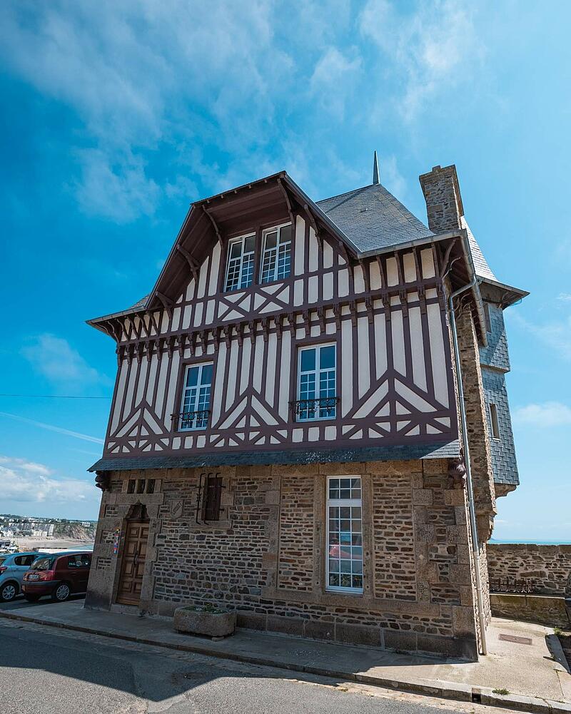 [Translate to Allemand:] A beautiful historic building combining a stone ground floor with upper levels featuring traditional half-timbered architecture, discovered while staying at Les Castels.