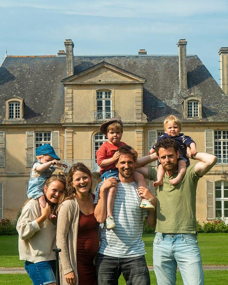 [Translate to Allemand:] A joyful group photo of adults and young children smiling together in front of a historic French chateau at a luxury Les Castels holiday estate.